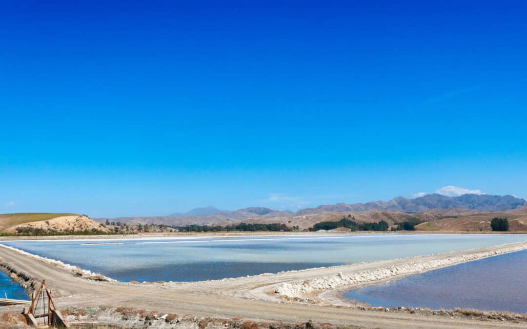 Aerial view of mine evaporation ponds and processing infrastructure under a clear blue sky.