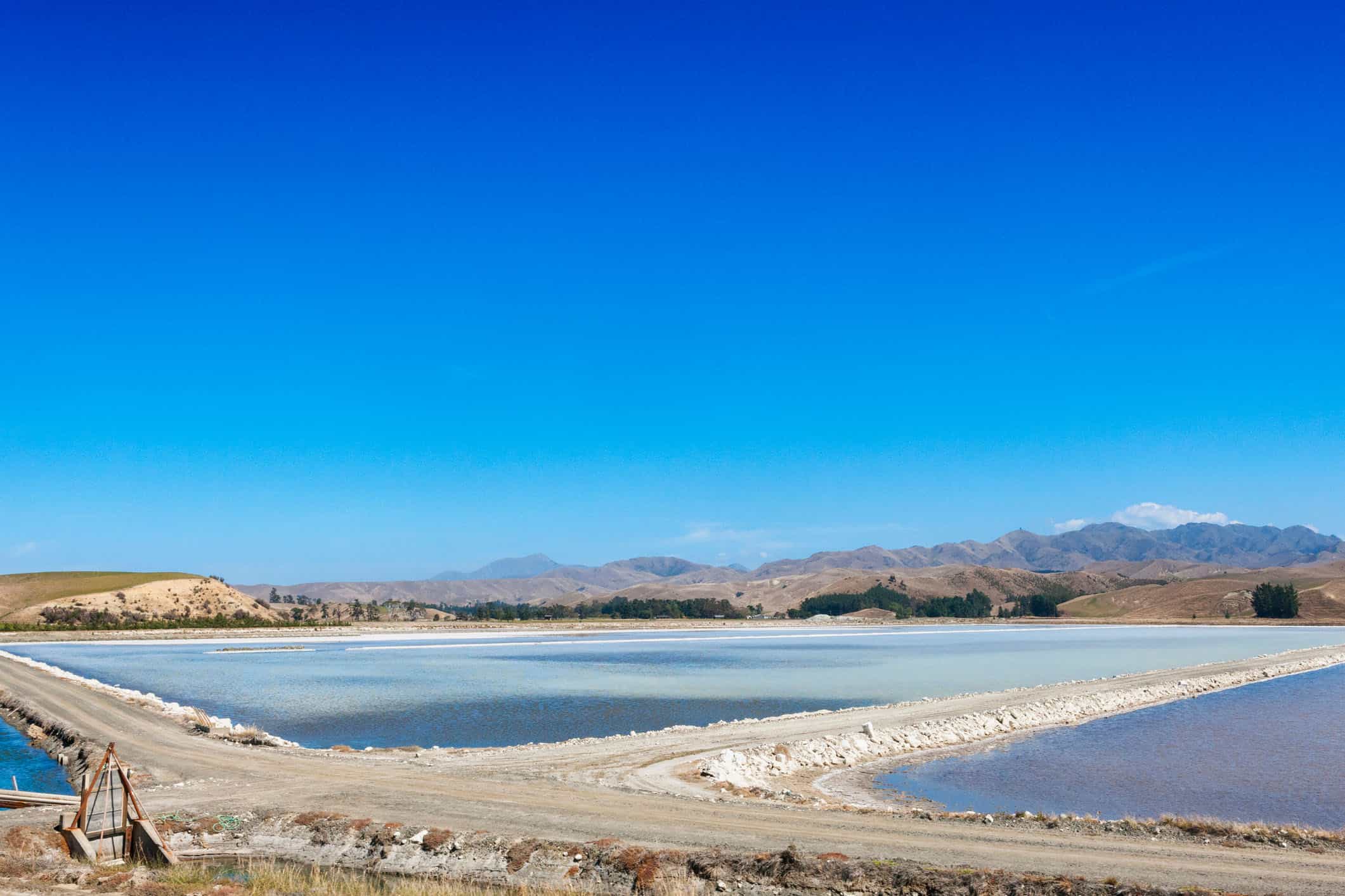 Aerial view of mine evaporation ponds and processing infrastructure under a clear blue sky.