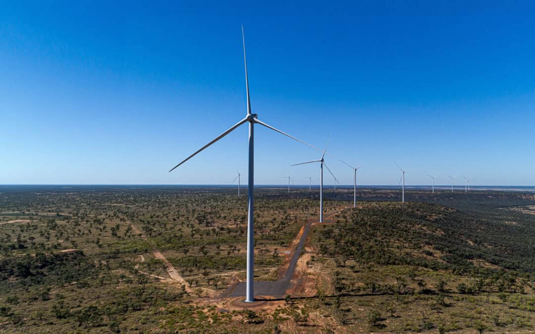 Wind turbines in a flat, arid landscape beneath a clear blue sky.