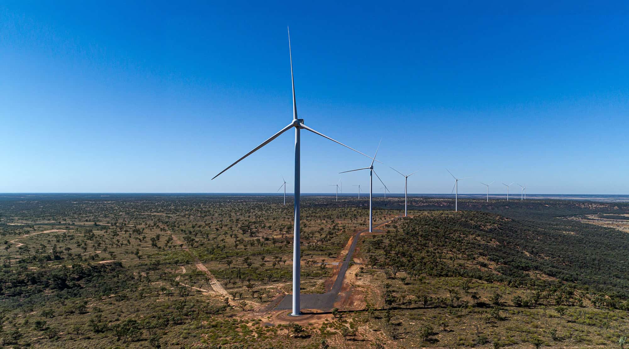 Wind turbines in a flat, arid landscape beneath a clear blue sky.