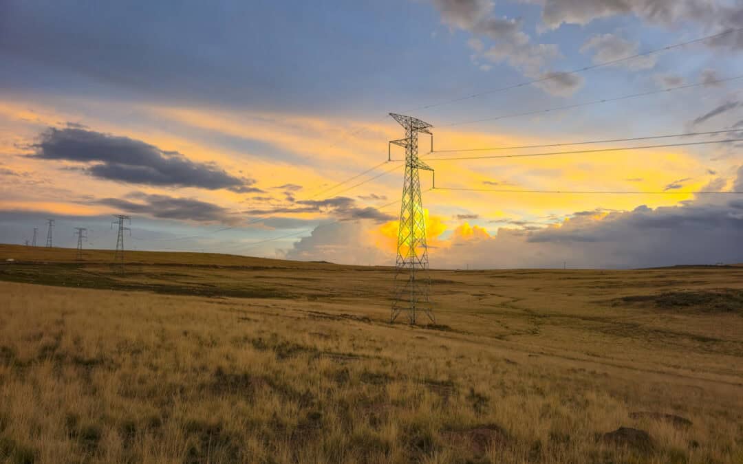 High-voltage transmission towers crossing a rural landscape at sunset.