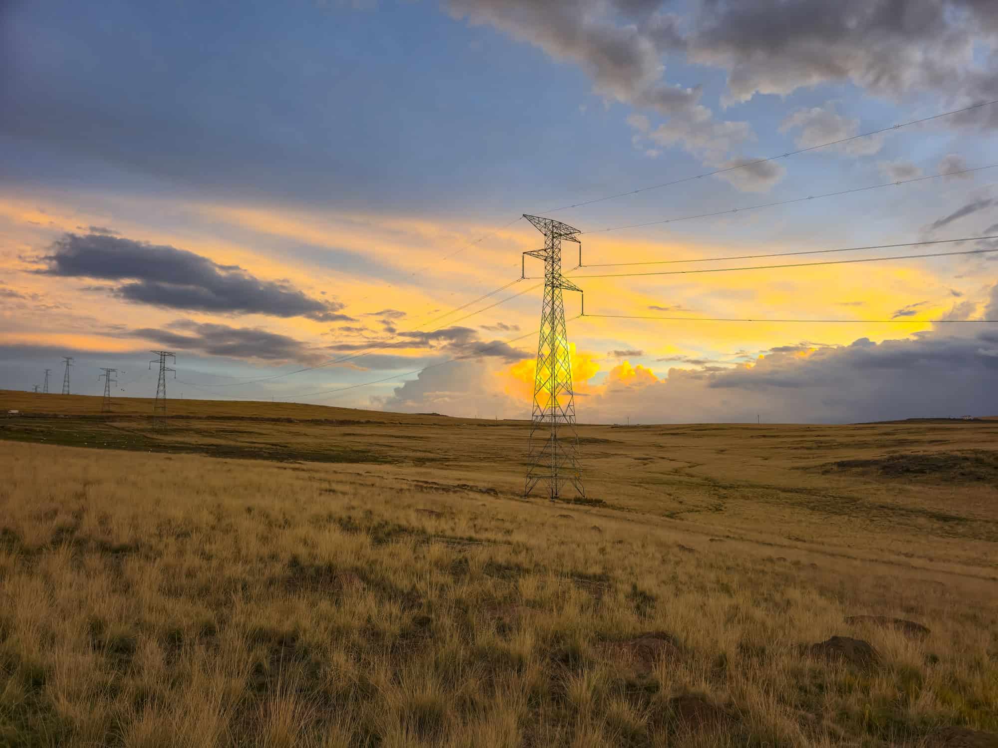 High-voltage transmission towers crossing a rural landscape at sunset.